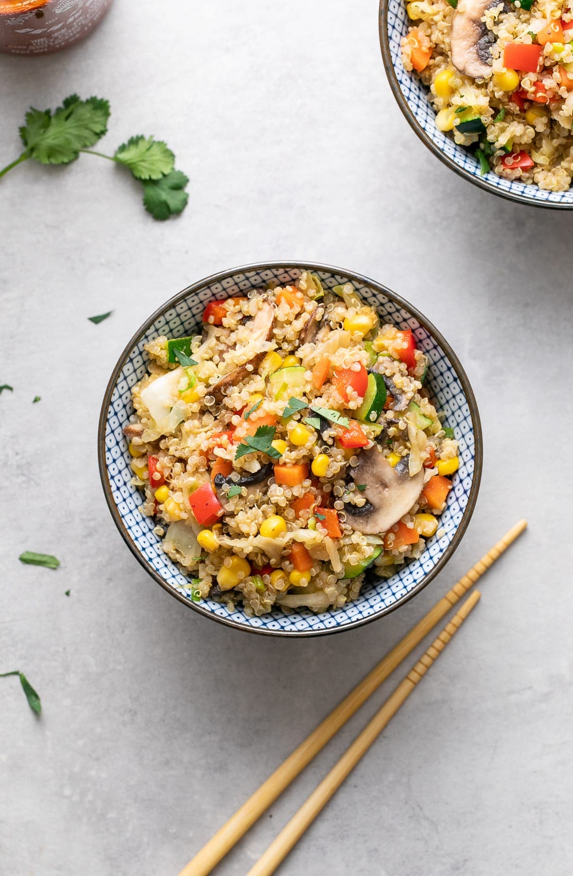 top down view of vegetable quinoa fried rice in a blue and white bowl with items surrounding.