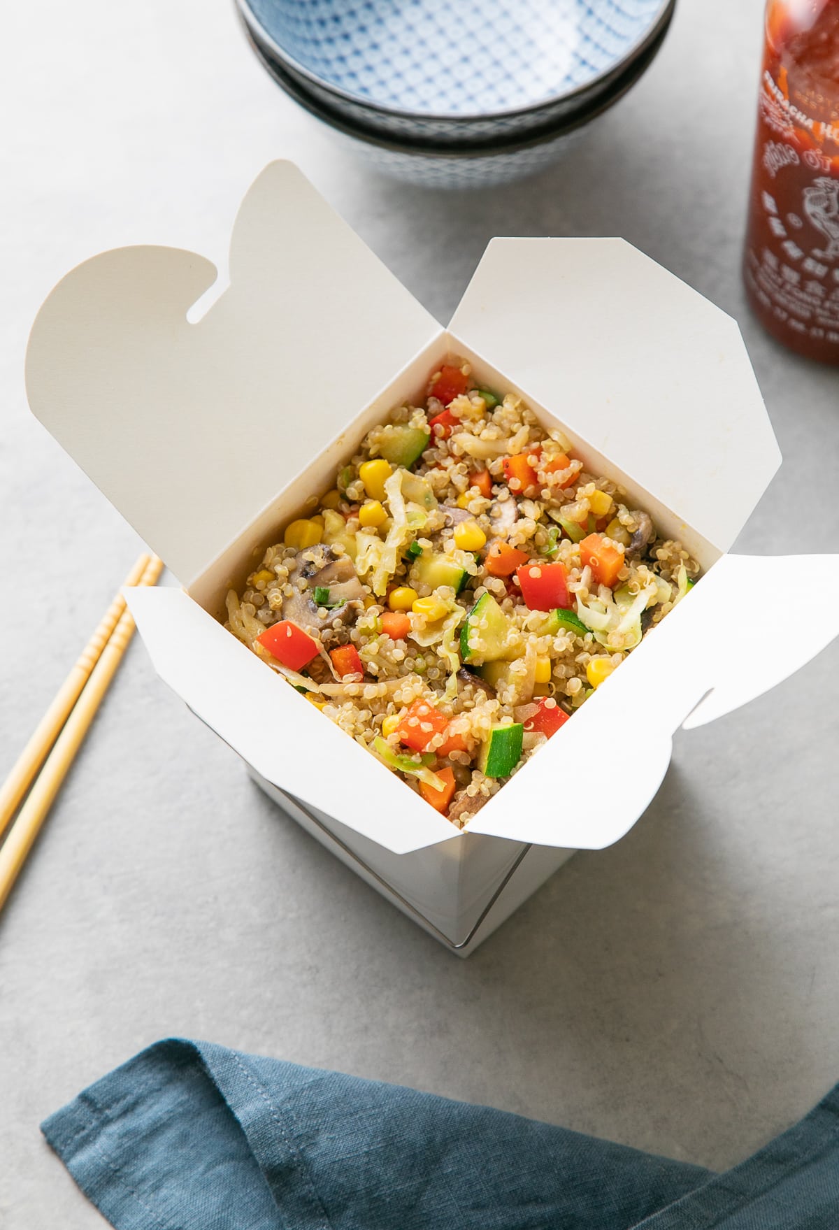 vegetable quinoa fried rice in a chinese take out box with items surrounding.