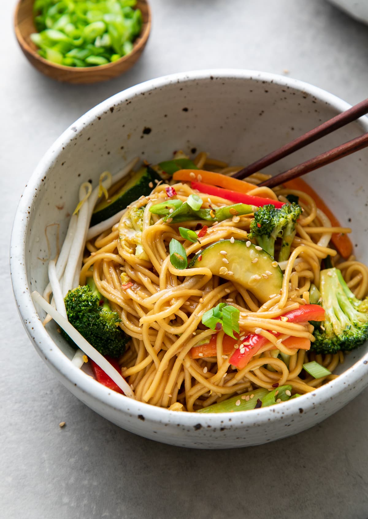 side angle view of bowl with veggie ramen noodle stir fry with items surrounding.