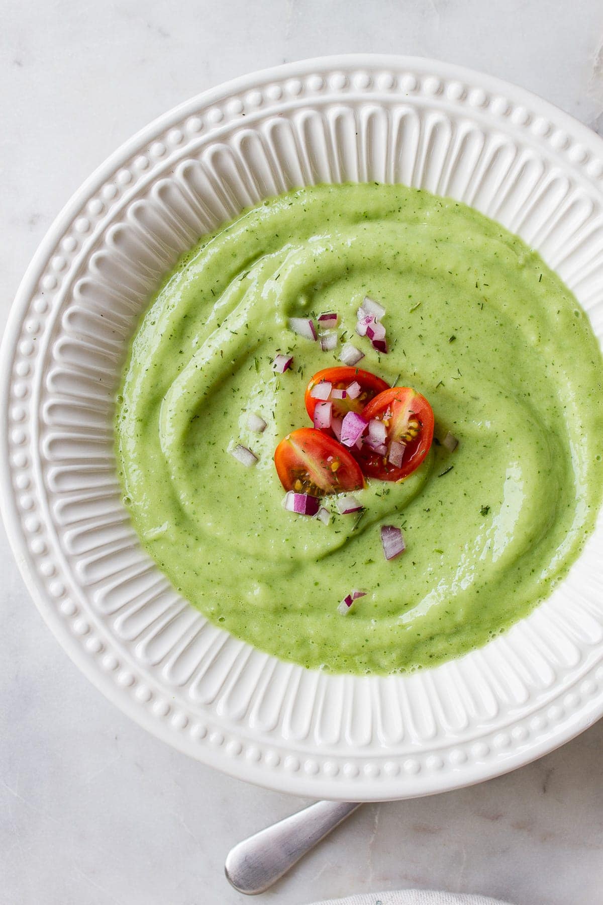 top down view of a white bowl with a serving of easy vegan chilled avocado cucumber soup.