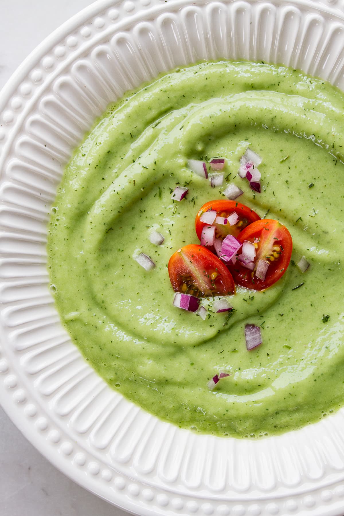 top down view of a white bowl with a serving of easy vegan chilled avocado cucumber soup.