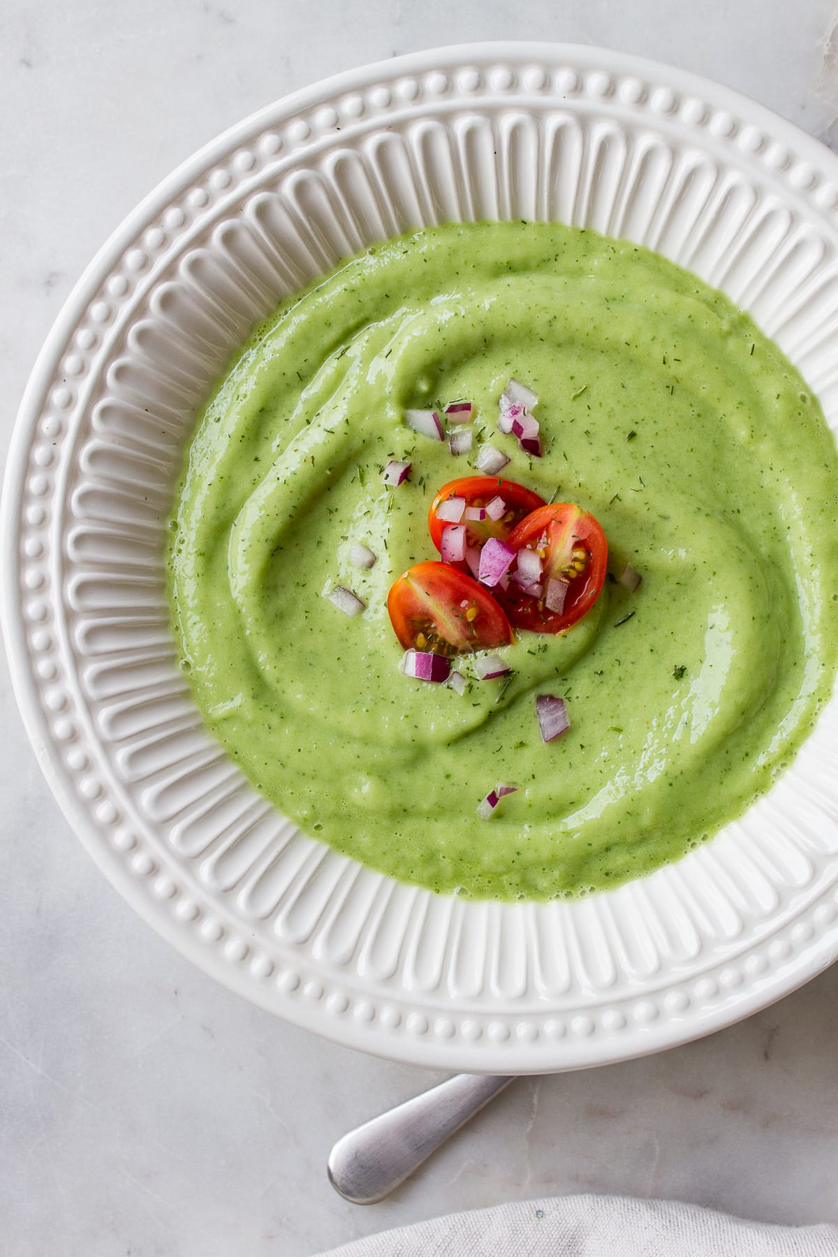 top down view of a white bowl with a serving of easy vegan chilled avocado cucumber soup.