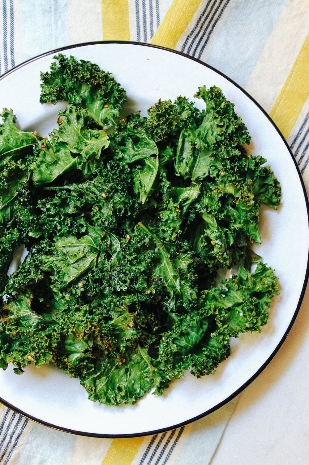 crispy baked kale chips on a white round plate with black rim