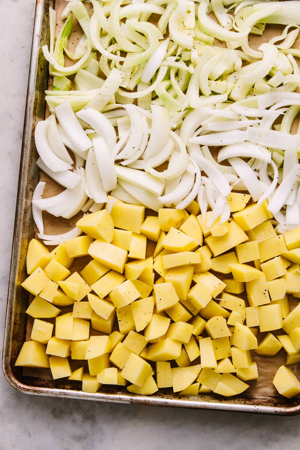 top down view of prepped fennel, onion and potatoes on a rimmed baking sheet.