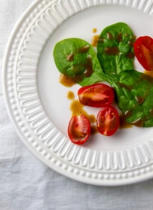 top down view of a small white plate with spinach and tomatoes drizzled with healthy flax & evo balsamic vinaigrette.
