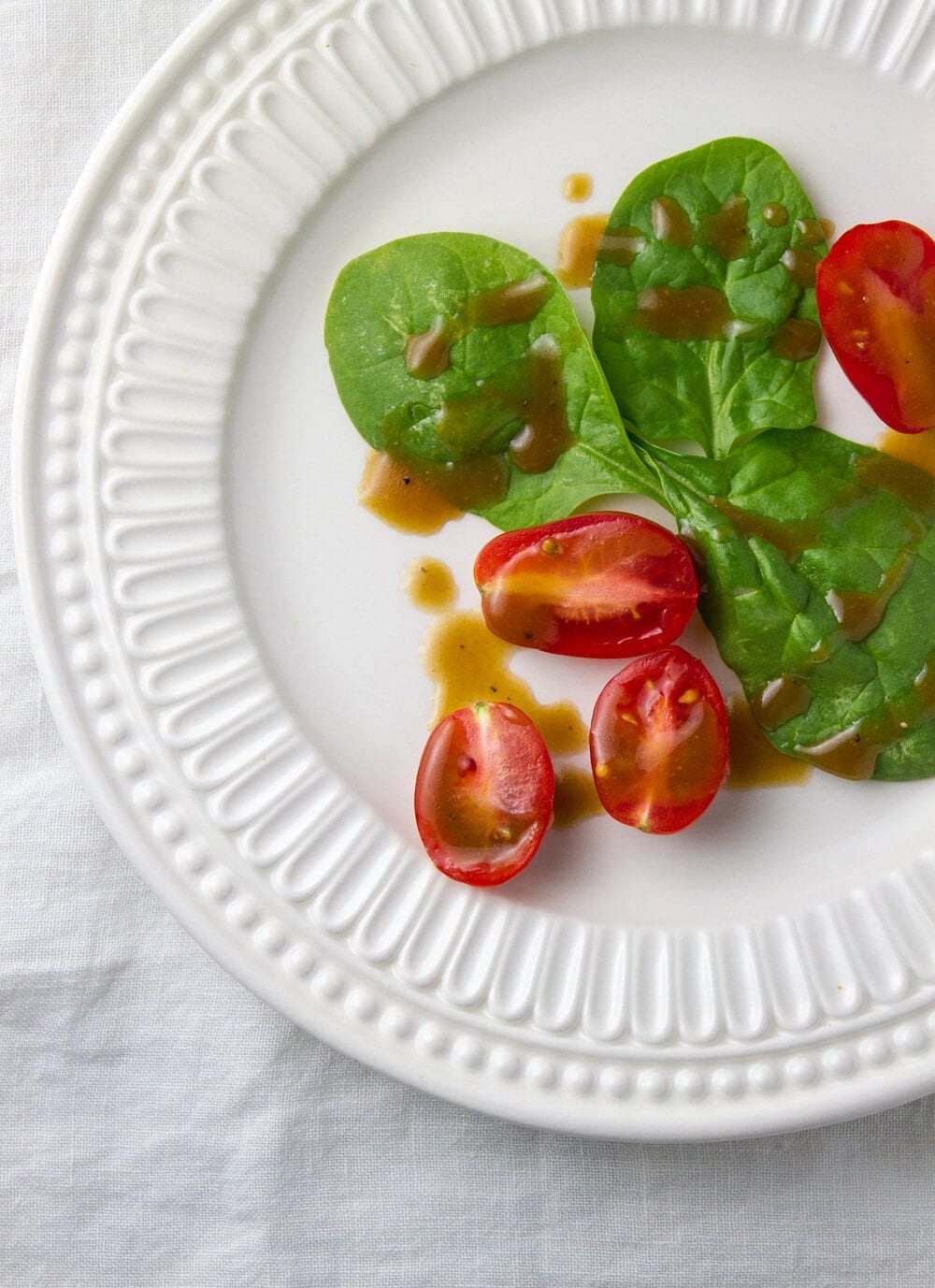 top down view of a small white plate with spinach and tomatoes drizzled with healthy flax & evo balsamic vinaigrette.