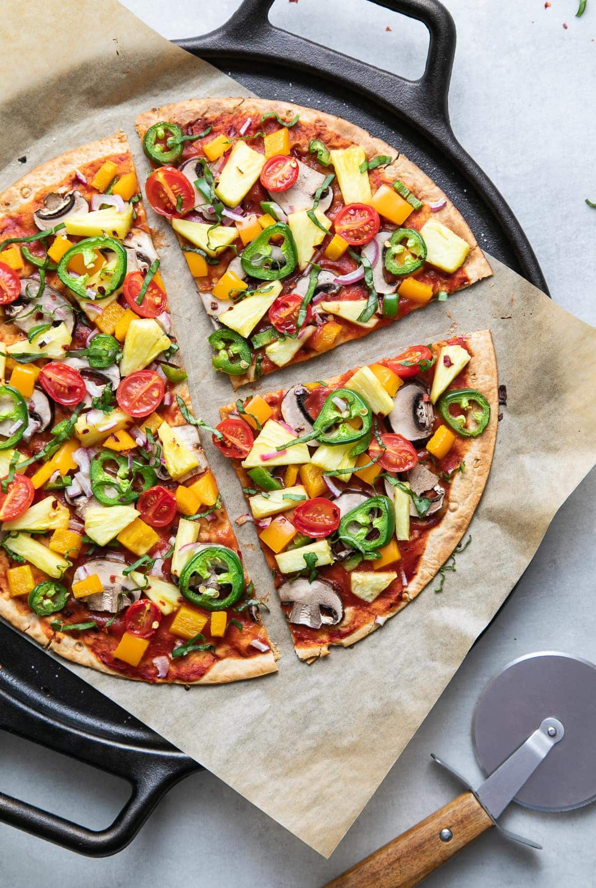 top down view of freshly baked pineapple veggie lovers pizza on a cast iron pizza pan sliced.