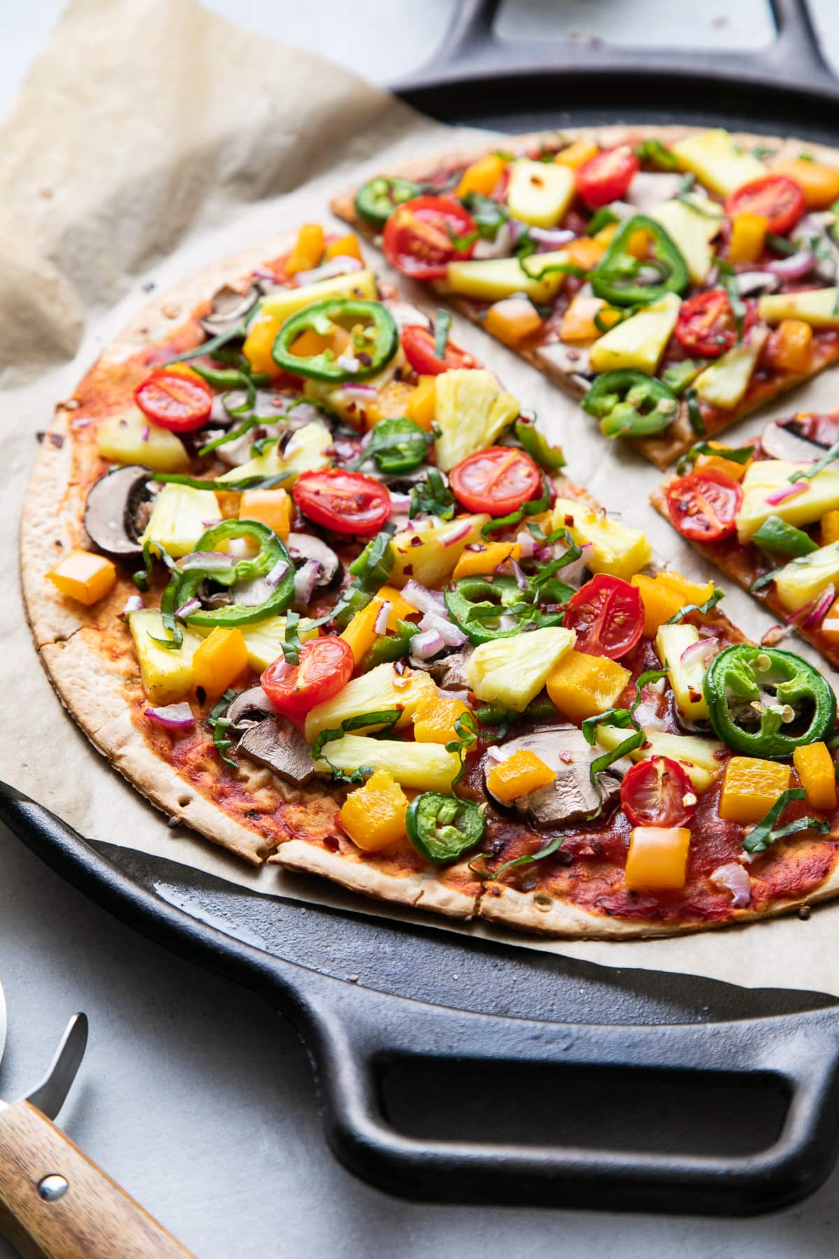 side angle view of freshly baked pineapple veggie lovers pizza on a cast iron pizza pan sliced.