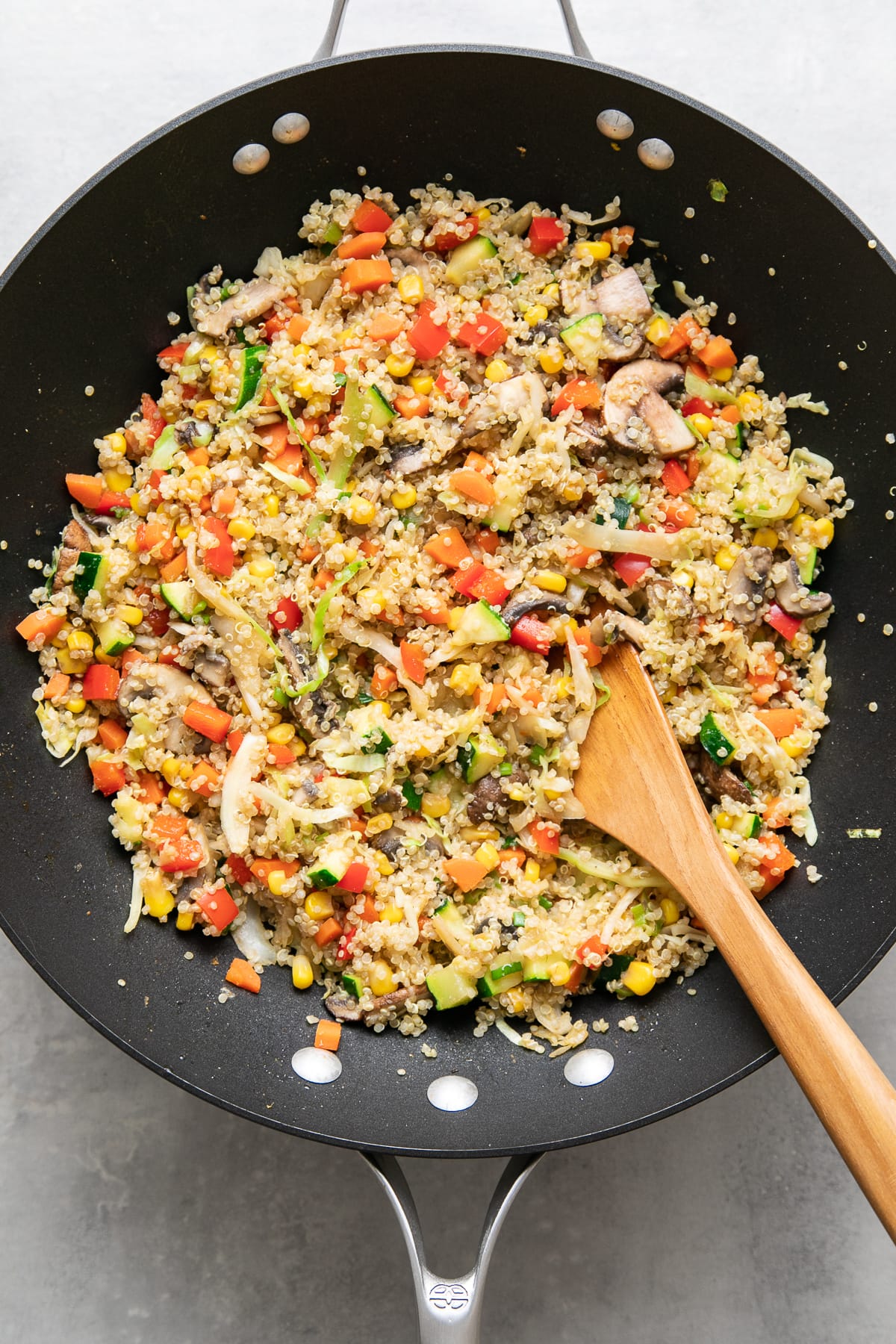 top down view of freshly made quinoa fried rice in a wok with wooden spoon.