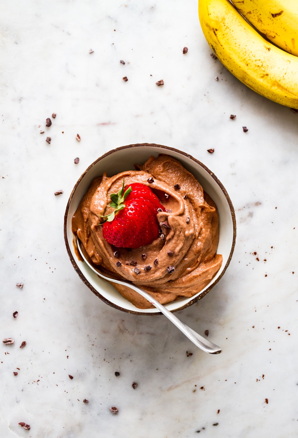 top down view of a bowl with raw vegan chocolate banana ice cream with sliced strawberry and a spoon.