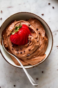 top down view of a bowl with raw vegan chocolate banana ice cream with sliced strawberry and a spoon.