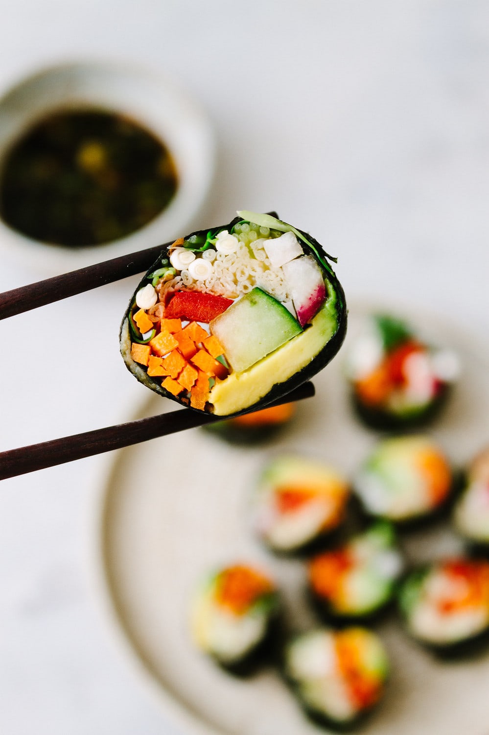 side angle shot of a slice of raw vegan sushi roll between 2 chopsticks