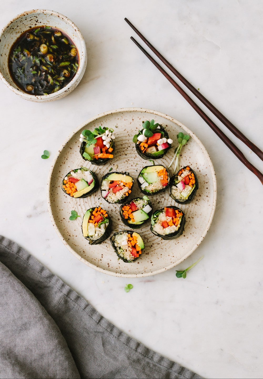 top down view of sushi roll cut up and placed on a small plate with bowl of dipping sauce, chopsticks and grey napkin