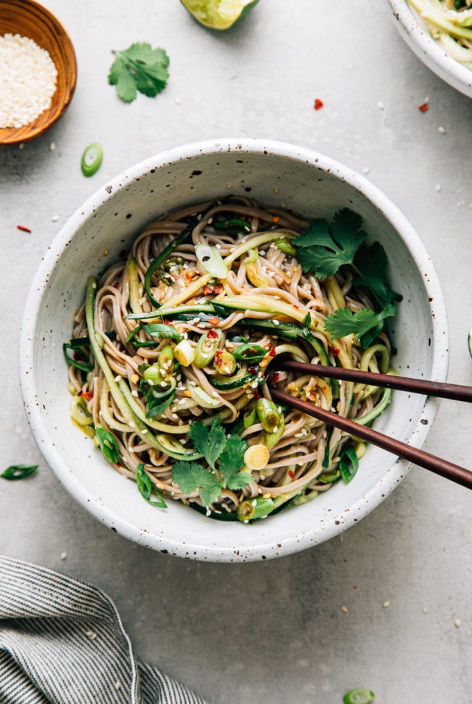 top down view of bowl with serving of soba noodle bowl with cucumber and sesame-ginger scallion sauce with chopsticks.
