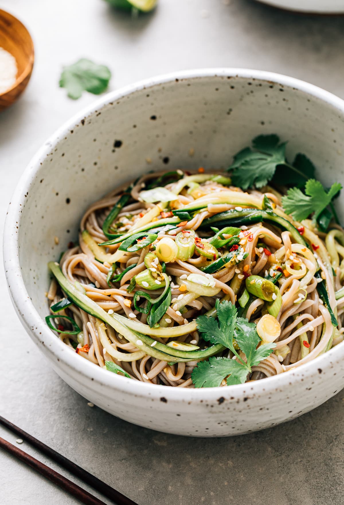 top down view of bowl with serving of soba noodle bowl with cucumber and sesame-ginger scallion sauce with items surrounding.