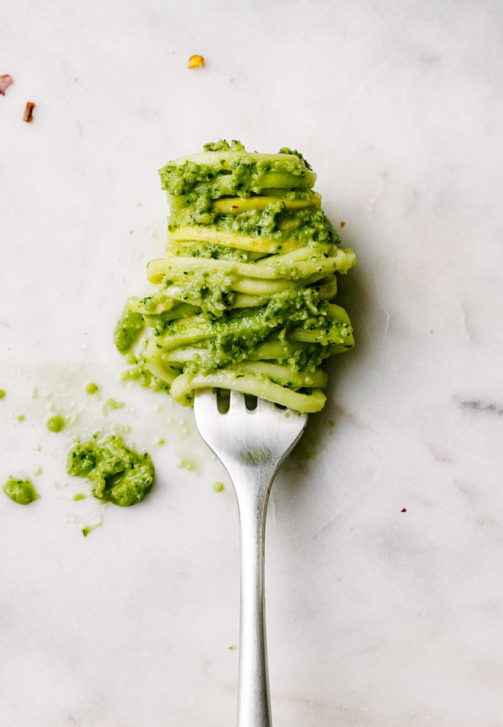 zucchini pesto and noodles wrapped around a fork on a marble slab