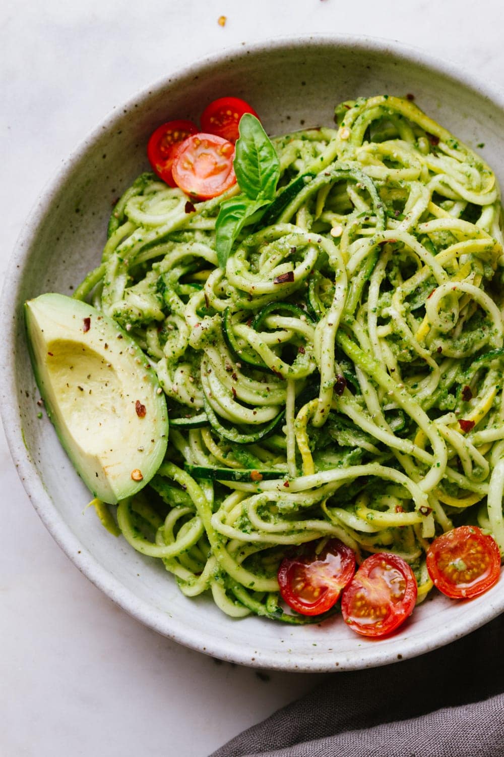 top down view of zucchini noodles with vegan zucchini pesto in a bowl with cherry tomatoes and avocado
