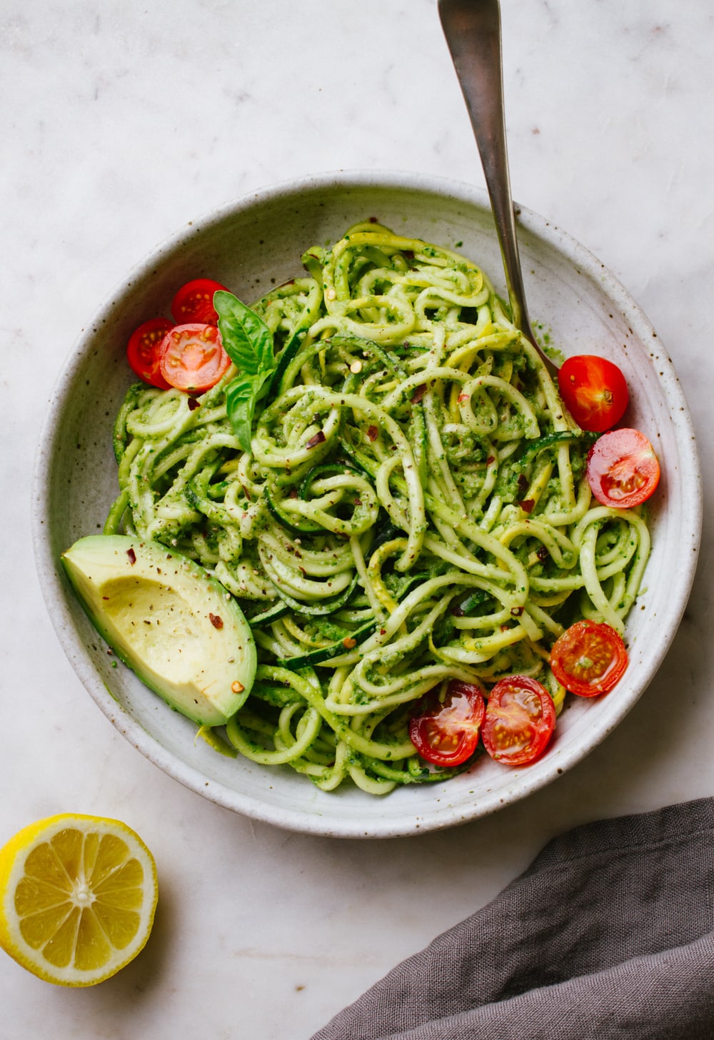 top down view of zucchini noodles with vegan zucchini pesto in a bowl with cherry tomatoes and avocado