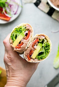 top down view of hand holding refried bean avocado lavash wrap sliced in half.