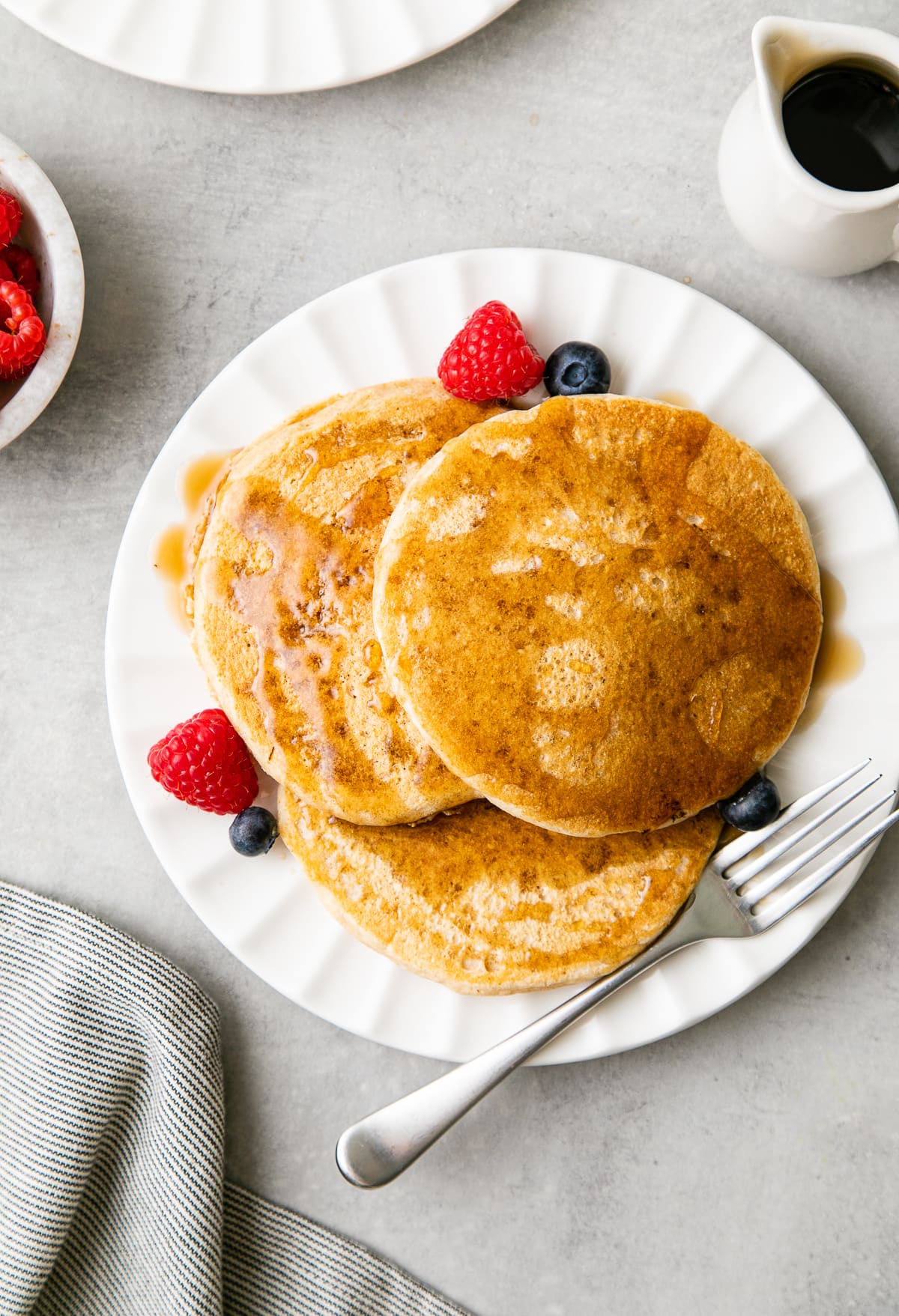 top down view of serving of vegan pancakes on a small plate with items surrounding.