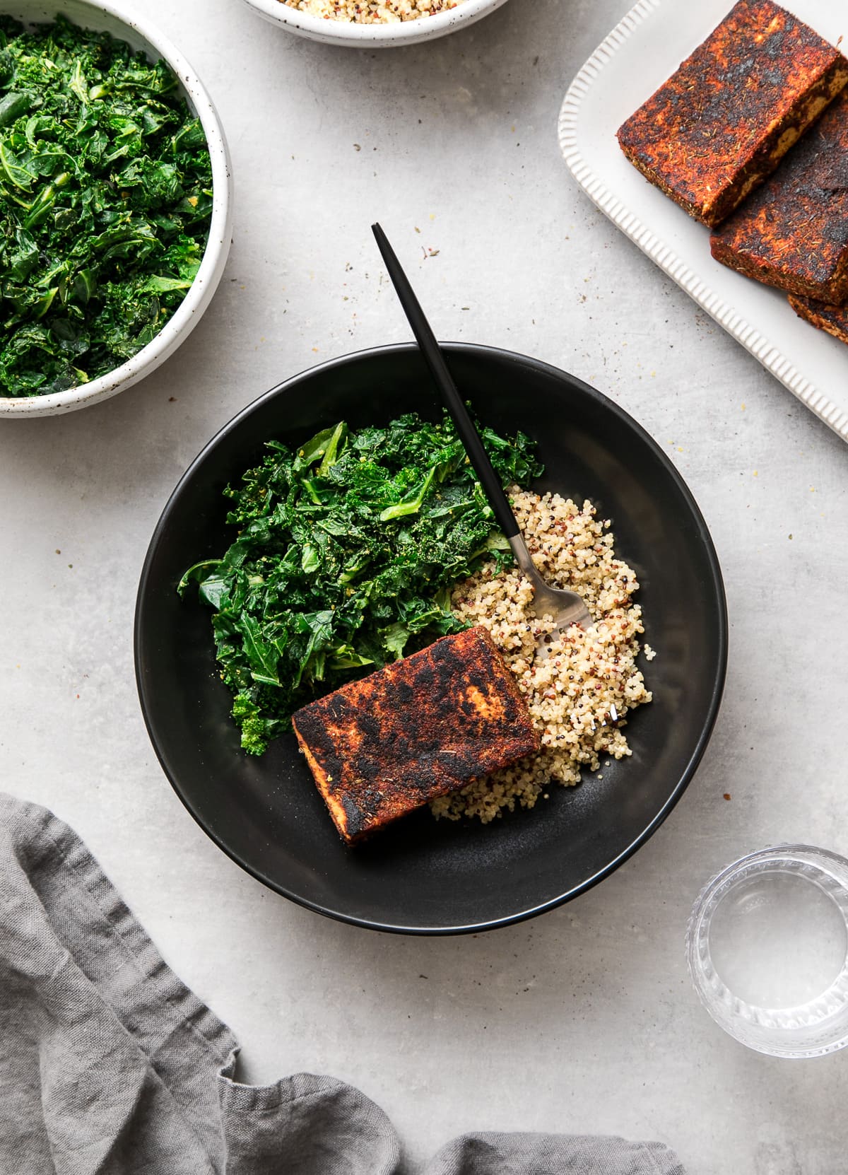 top down view of a black bowl with blackened tofu, sauteed kale and quinoa.