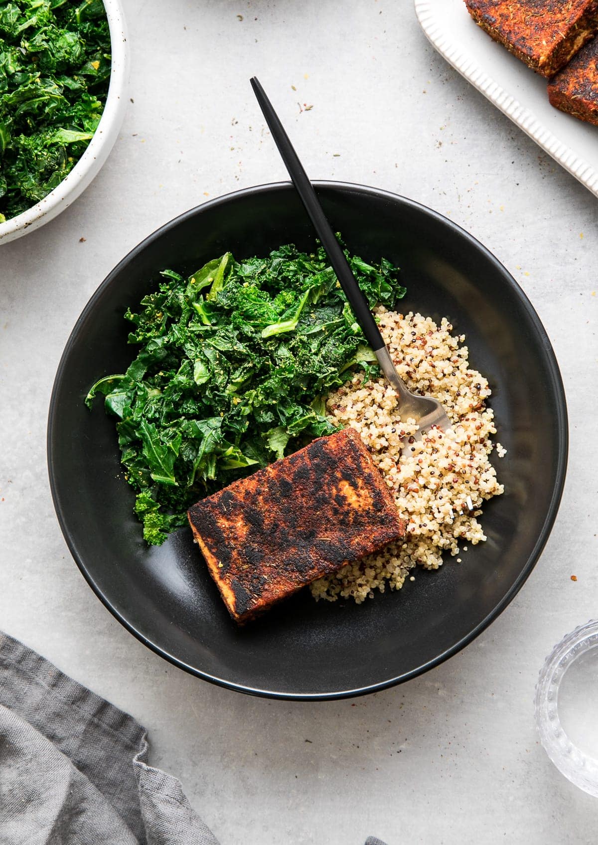 top down view of a black bowl with blackened tofu, sauteed kale and quinoa.