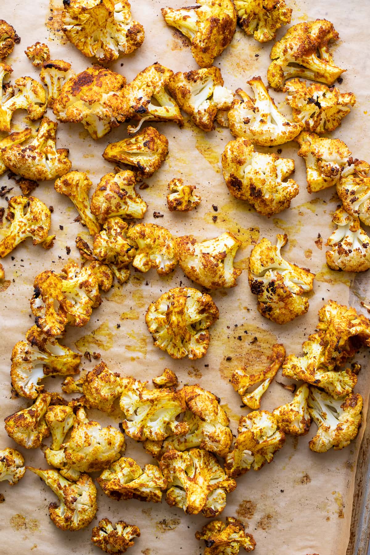 top down view of roasted cauliflower with curry and sriracha on a baking sheet just pulled from the oven.