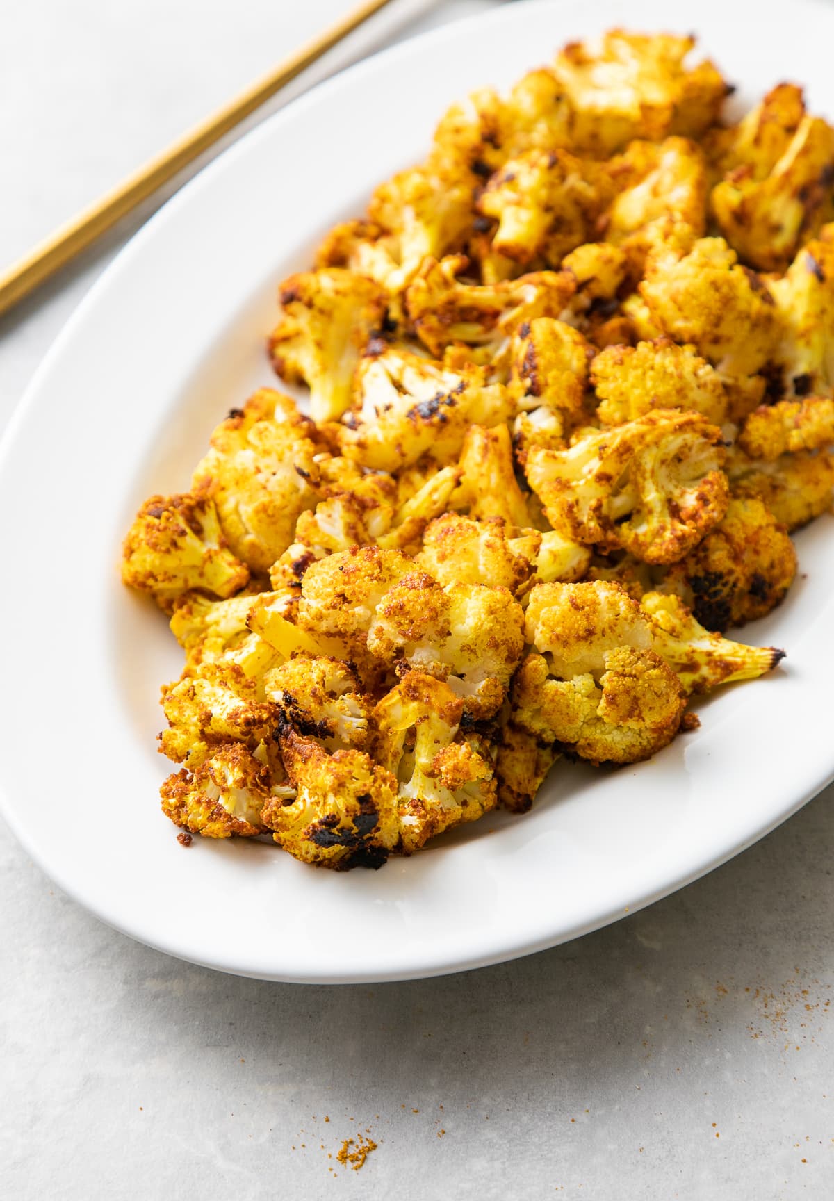 side angle view of a serving platter with freshly made curry sriracha roasted cauliflower.