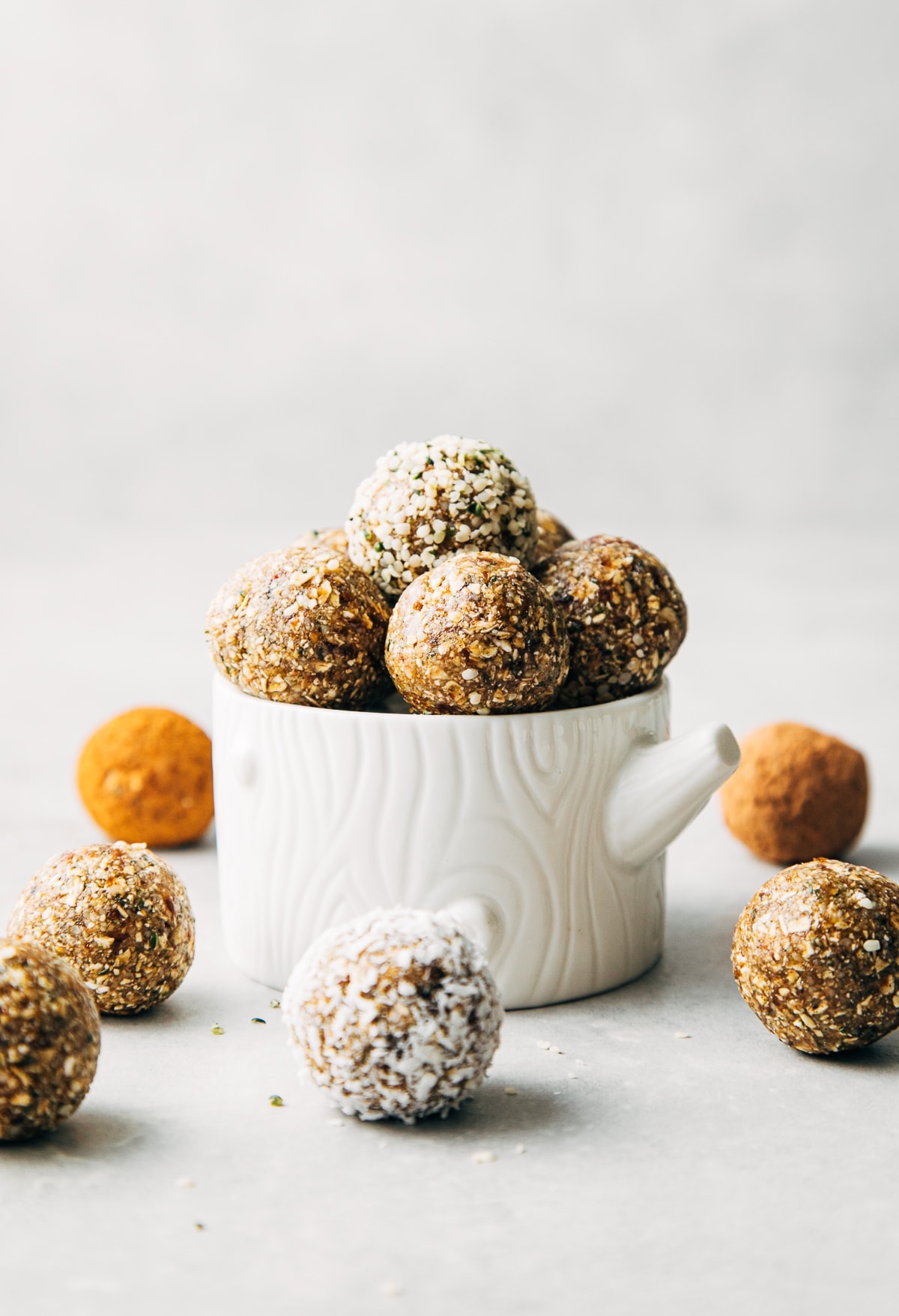 head on view of healthy raw oat and hemp heart energy bites in a small bowl with items surrounding.