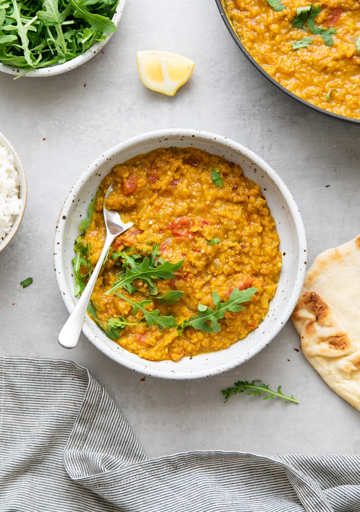top down view of healthy spicy red lentil dal in a bowl with spoon with items surrounding.
