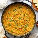 top down view of red lentil dahl in a cast iron pot with items surrounding.