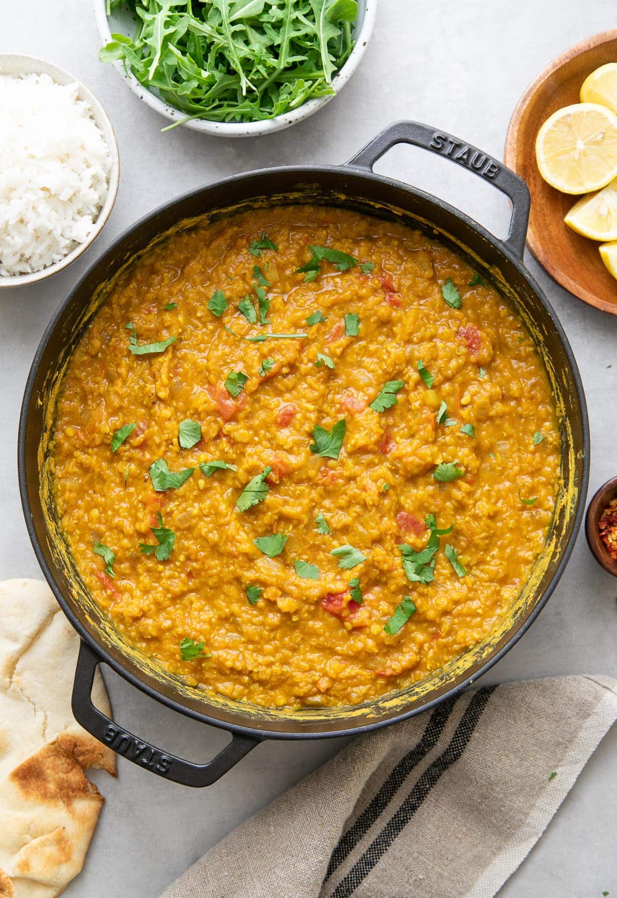top down view of red lentil dahl in a cast iron pot with items surrounding.