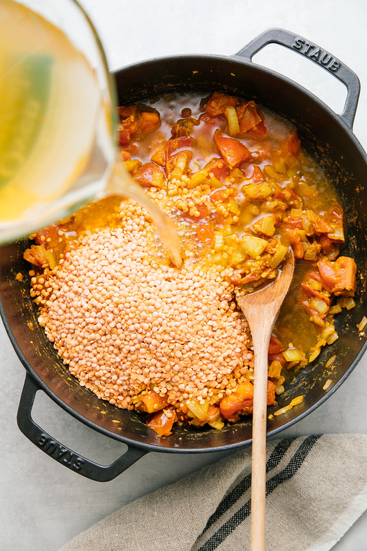 top down view of adding liquids and red lentils to pan to simmer.