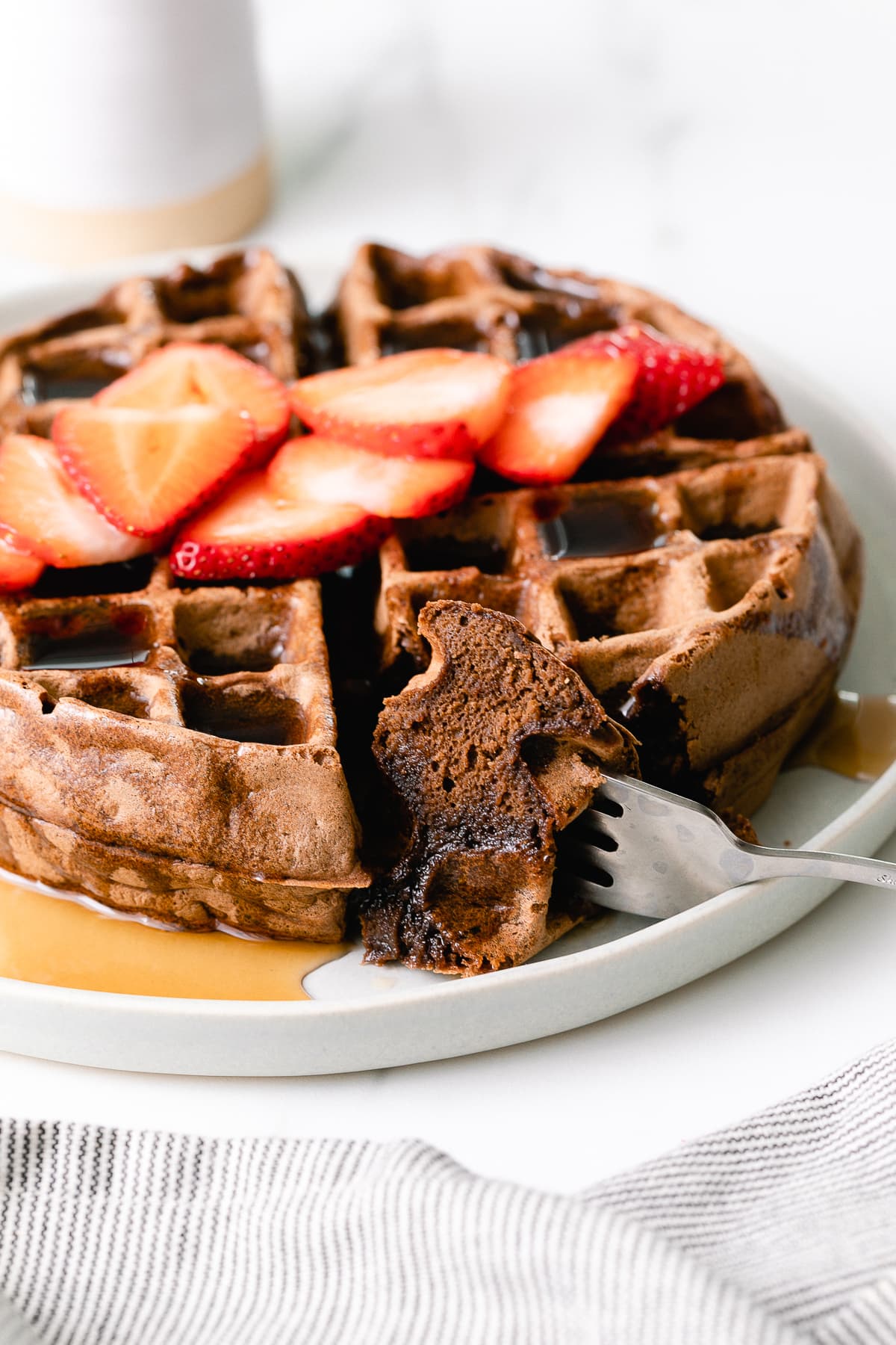 head on view of vegan chocolate belgian waffle on a plate with slice cut.