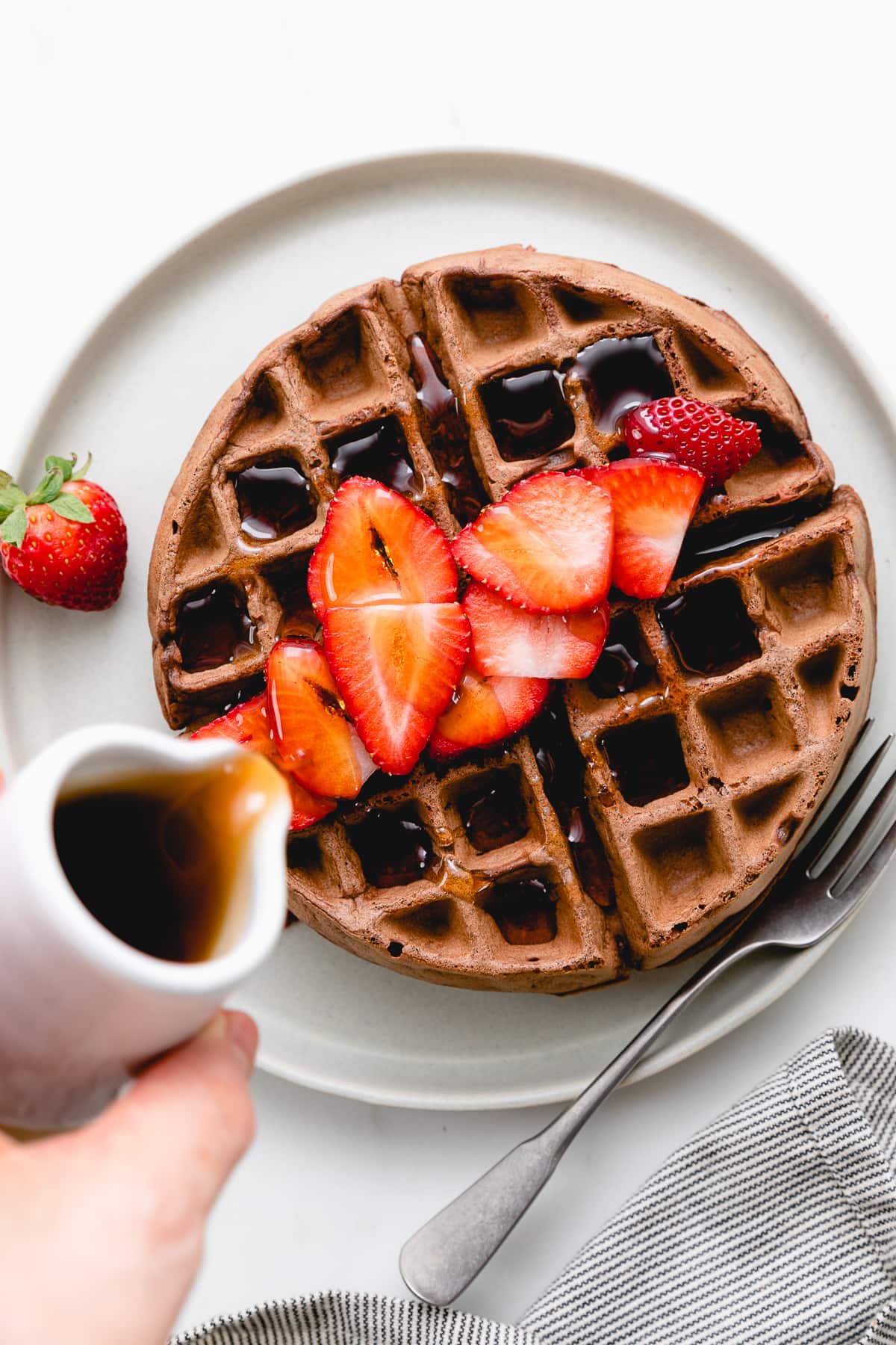 top down view of healthy vegan chocolate belgian waffle on a plate with syrup being poured overtop.