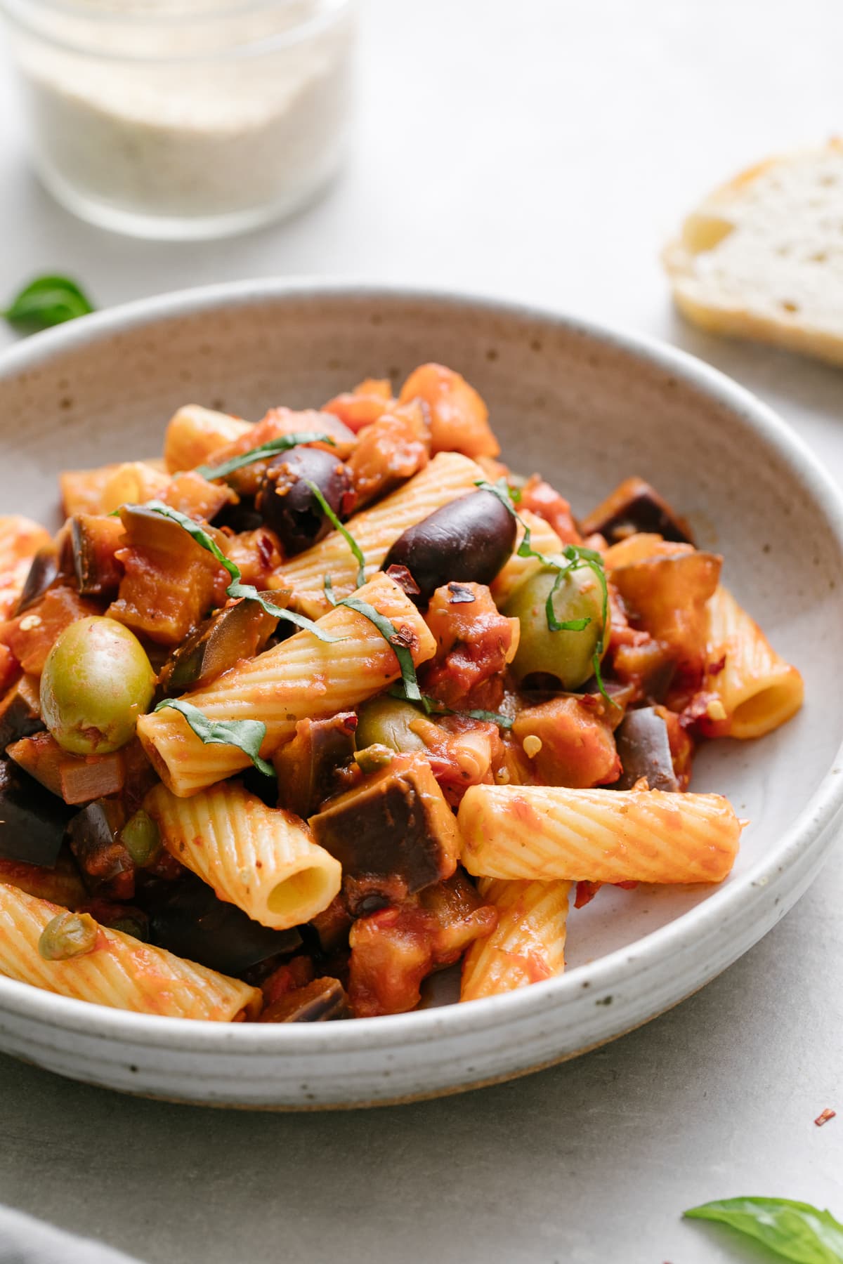 side angle view of a serving of eggplant puttanesca with pasta in a bowl with items surrounding.