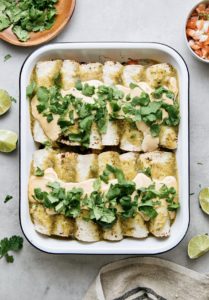 top down view of baking dish with homemade vegan enchiladas verde with items surrounding.