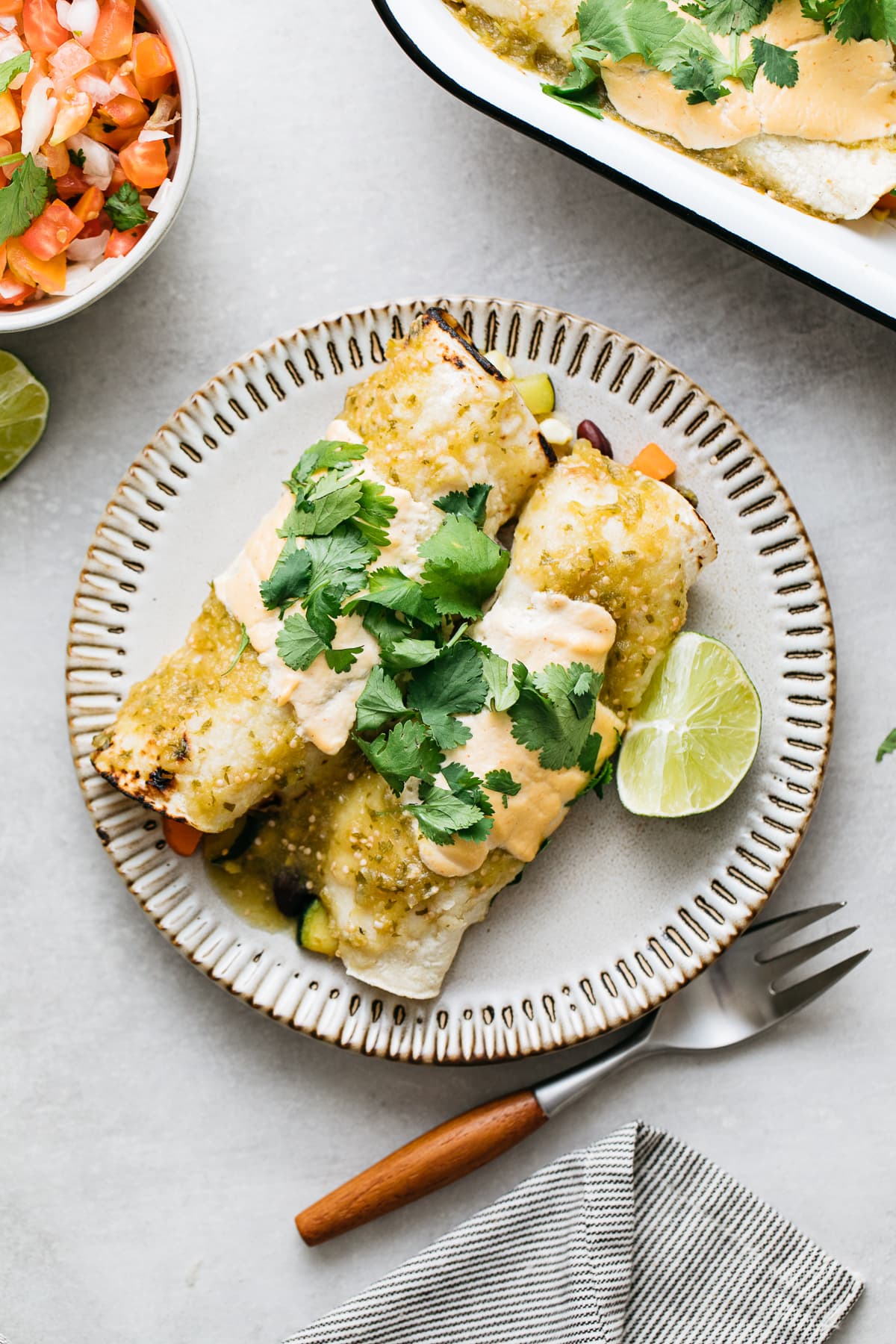 top down view of vegan enchilada verde on a small plate with items surroundings.