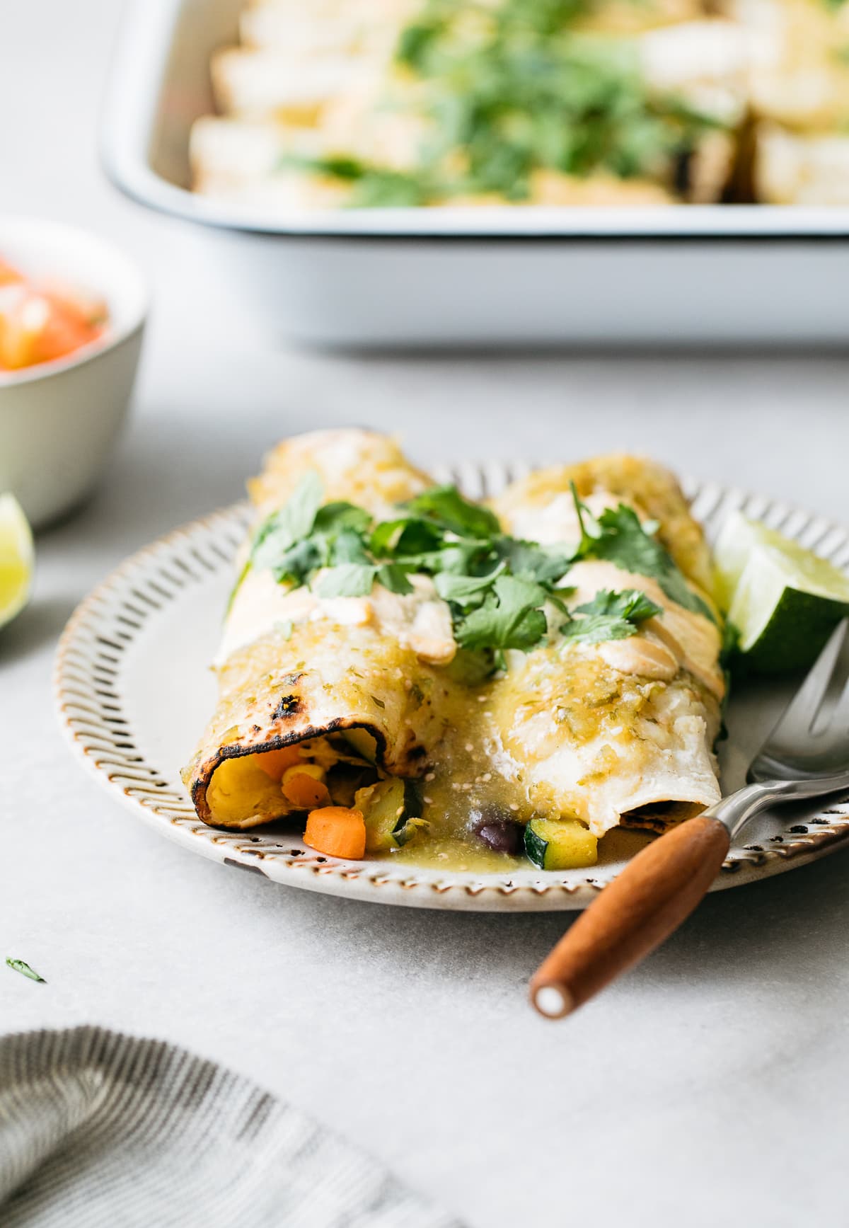 head on view of small plate with vegan enchiladas verde and items in the background.