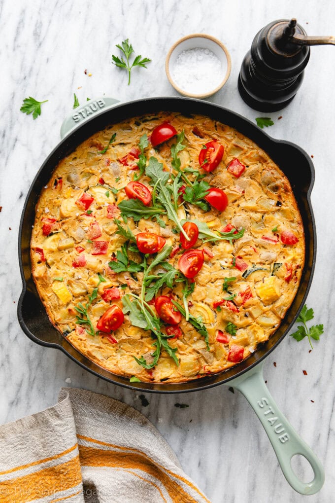 top down view of freshly baked vegan frittata on a marble slab with items surrounding.