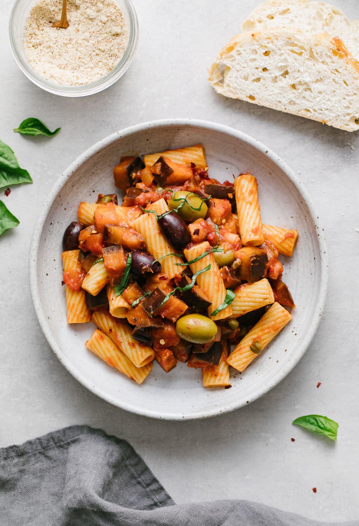 top down view of a serving of eggplant puttanesca with pasta in a bowl with items surrounding.