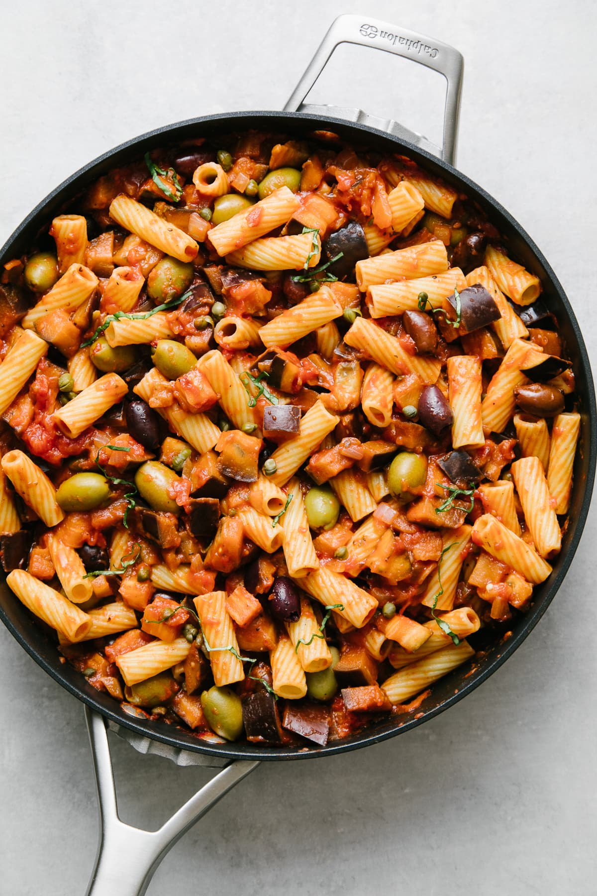 top down view of freshly made vegan eggplant puttanesca with pasta mixed in a skillet.