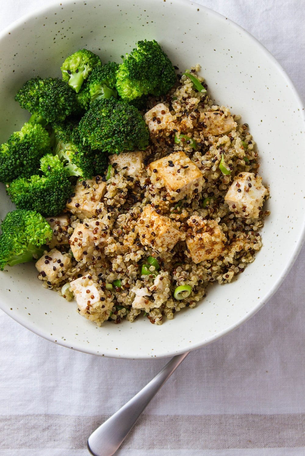 top down view of sesame quinoa and tofu with steamed broccoli in a bowl