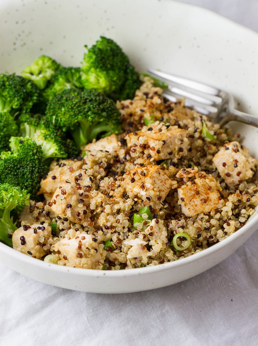 side angle view of sesame quinoa tofu with steamed broccoli in a bowl with fork