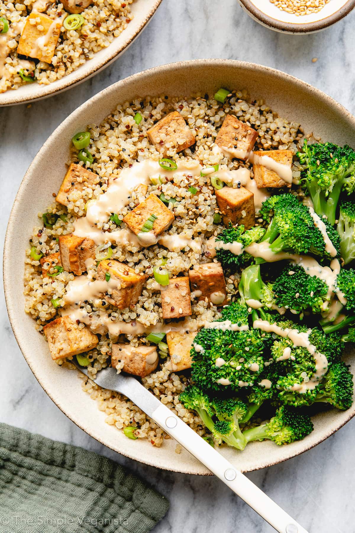 top down view of plated sesame quinoa and tofu bowl with broccoli and drizzle of spicy sauce.