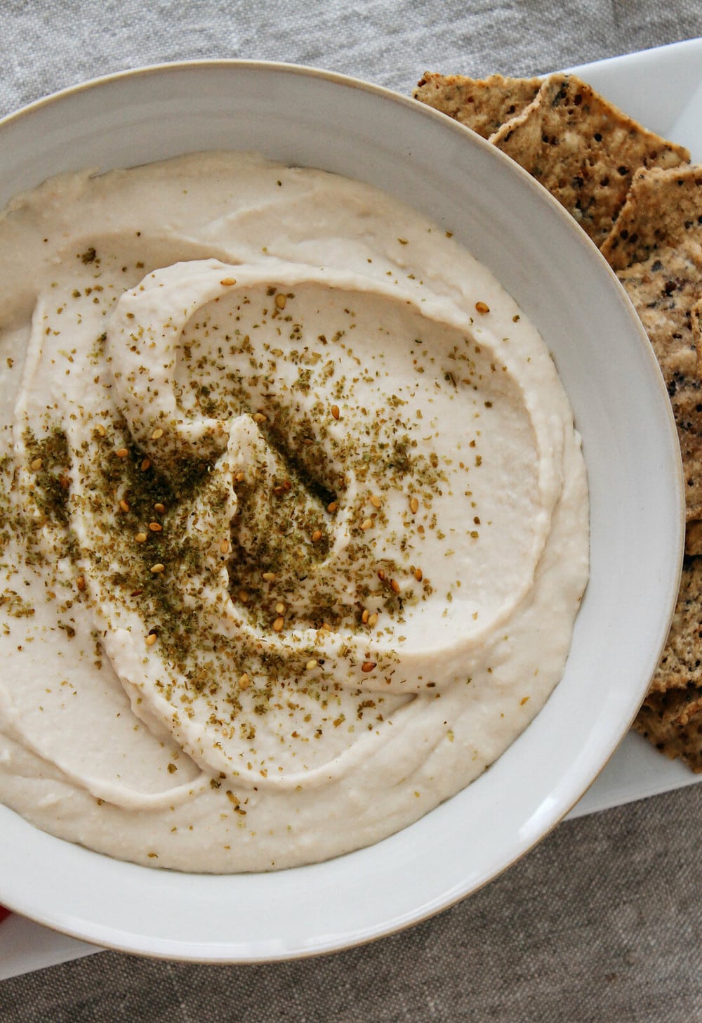 top down view of white bean hummus garnished with za'atar in a white bowl.