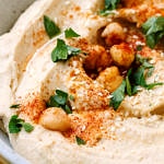up close view of creamy homemade hummus in a bowl, and garnished with chickpeas, parsley and paprika