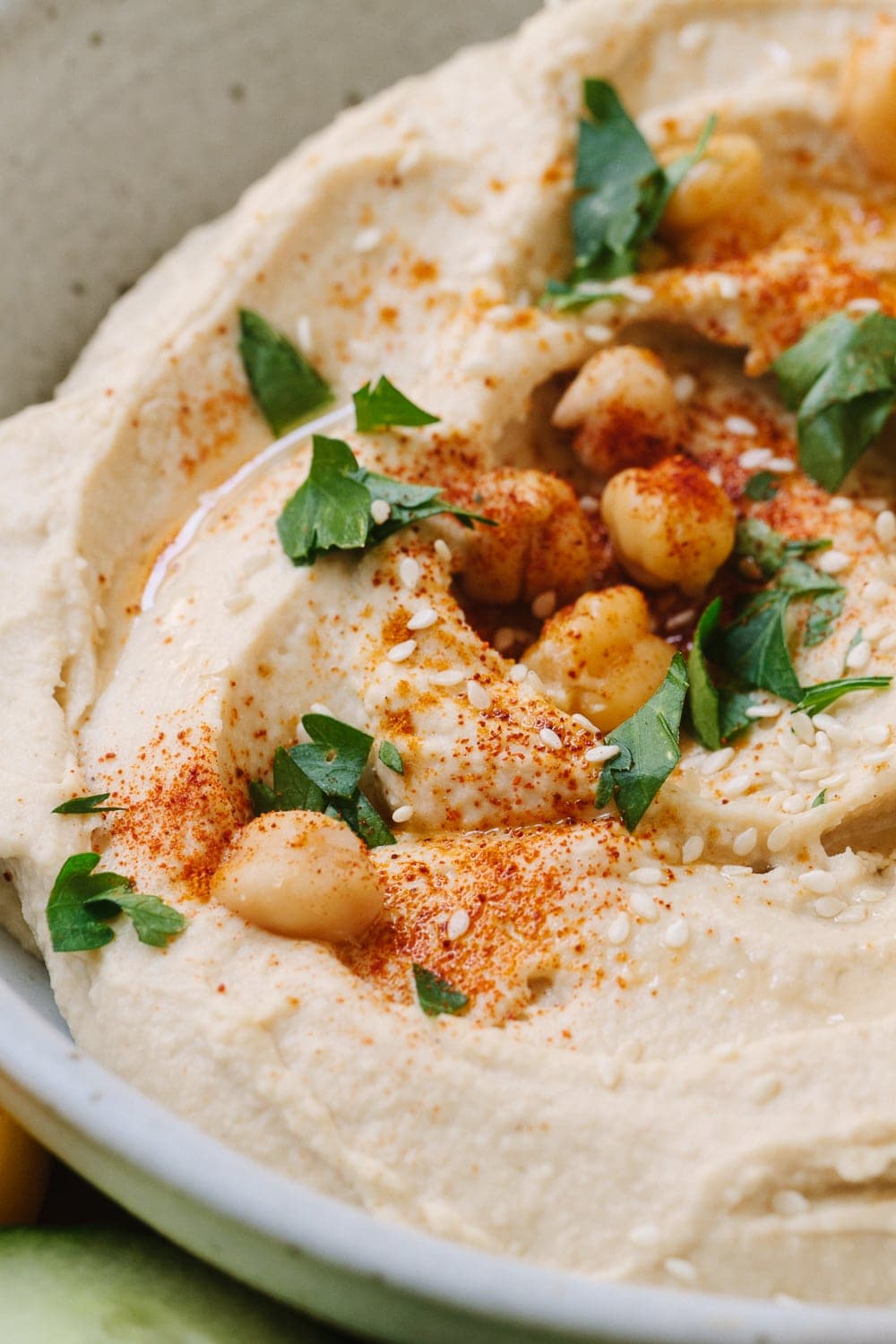 up close view of creamy homemade hummus in a bowl, and garnished with chickpeas, parsley and paprika