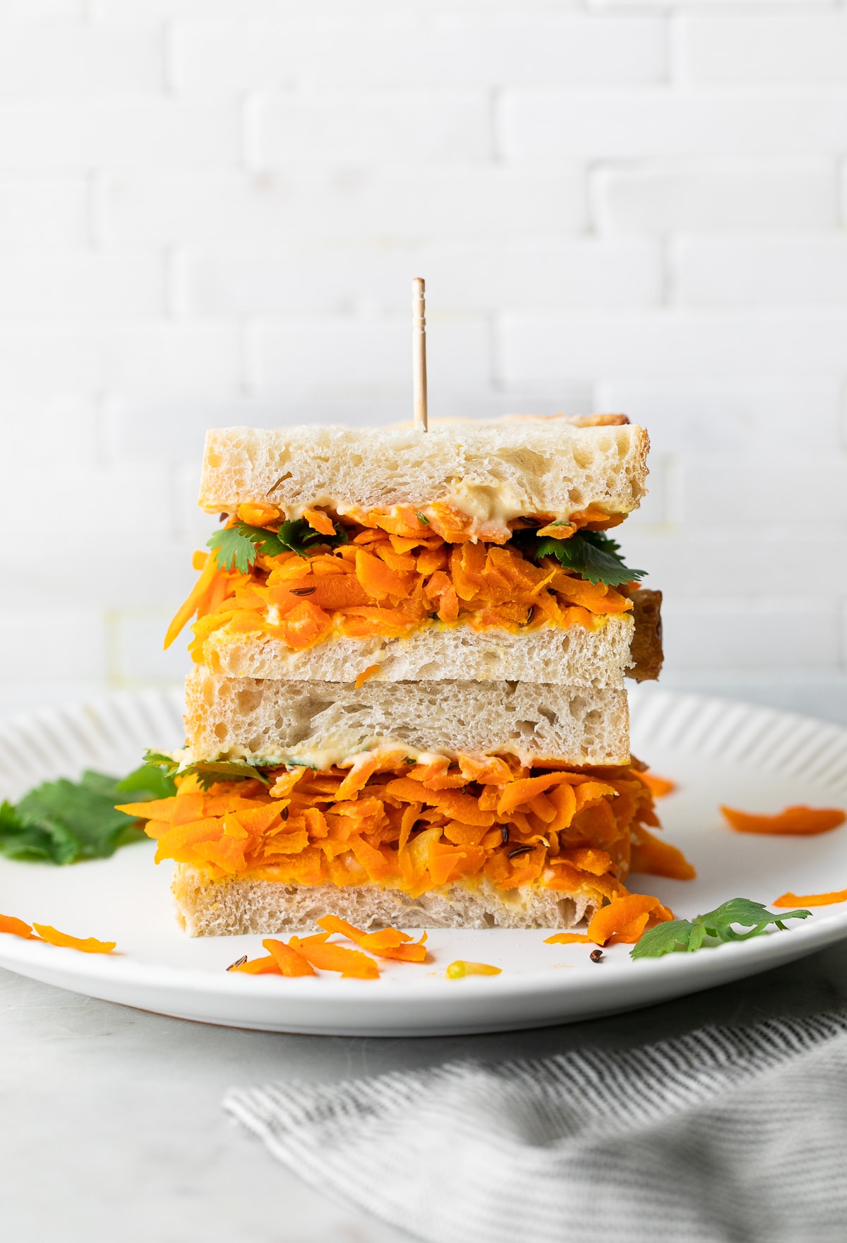 head on view of carrot and hummus sandwich sliced in half and stacked on a white plate.