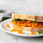 side angle view of carrot and hummus sandwich on a white plate.